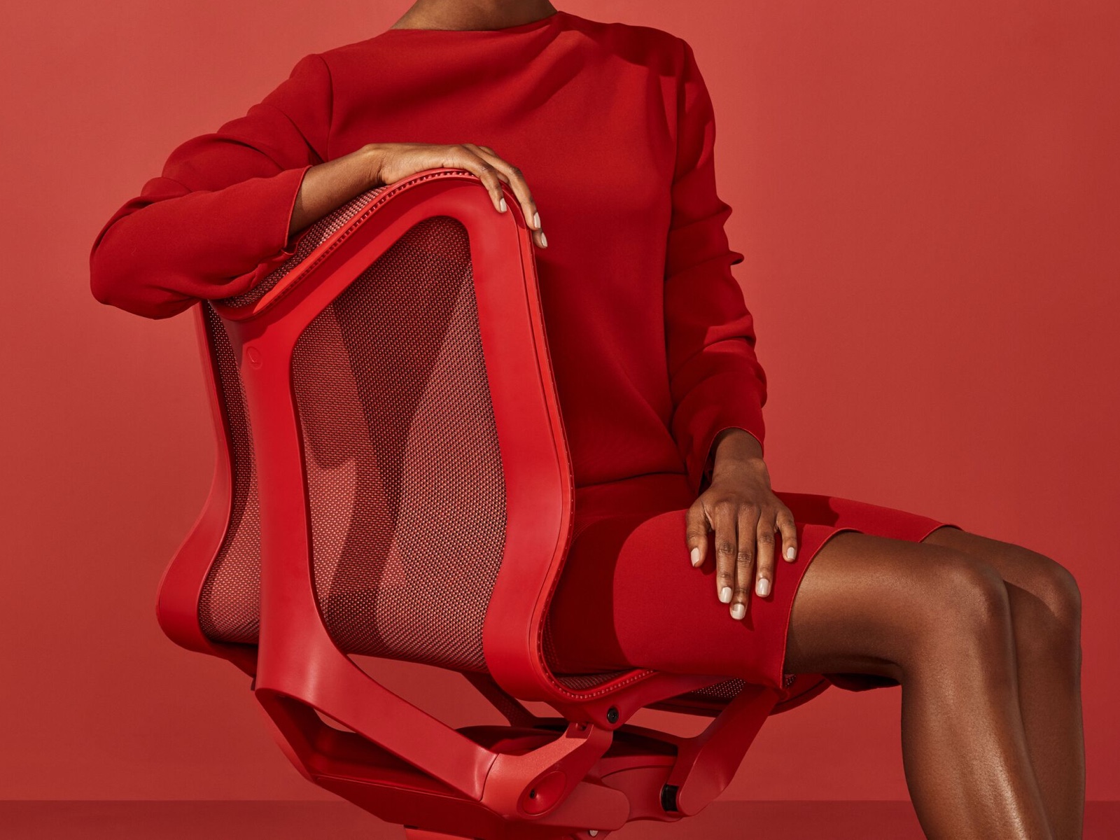 Una mujer con un vestido rojo se sienta en una silla Cosm con respaldo bajo en color rojo Canyon.