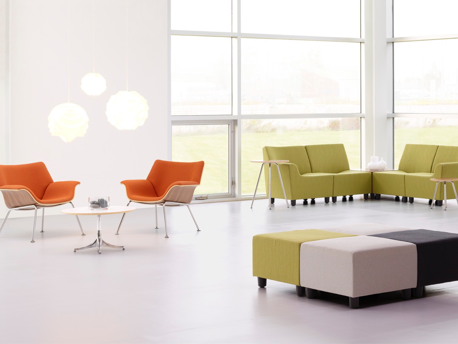 Sillones naranja Swoop y asientos modulares Shoop en verde en un espacio de reunión informal.